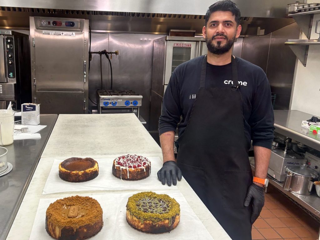 man in a kitchen standing by four creme cheesecakes