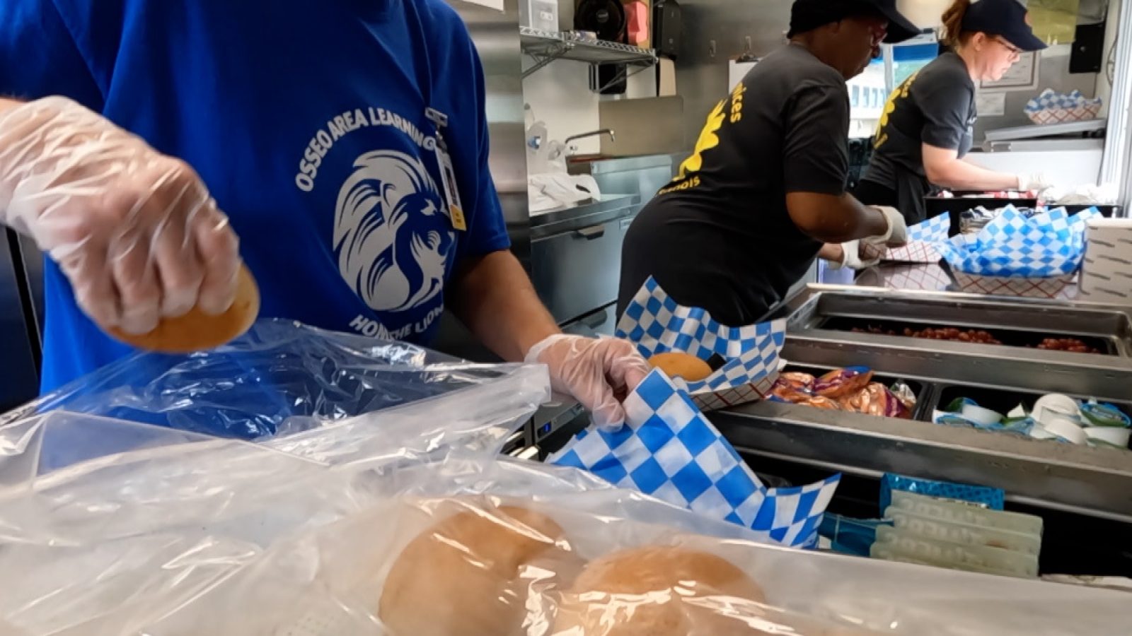 Three food service workers assemble to-go meals