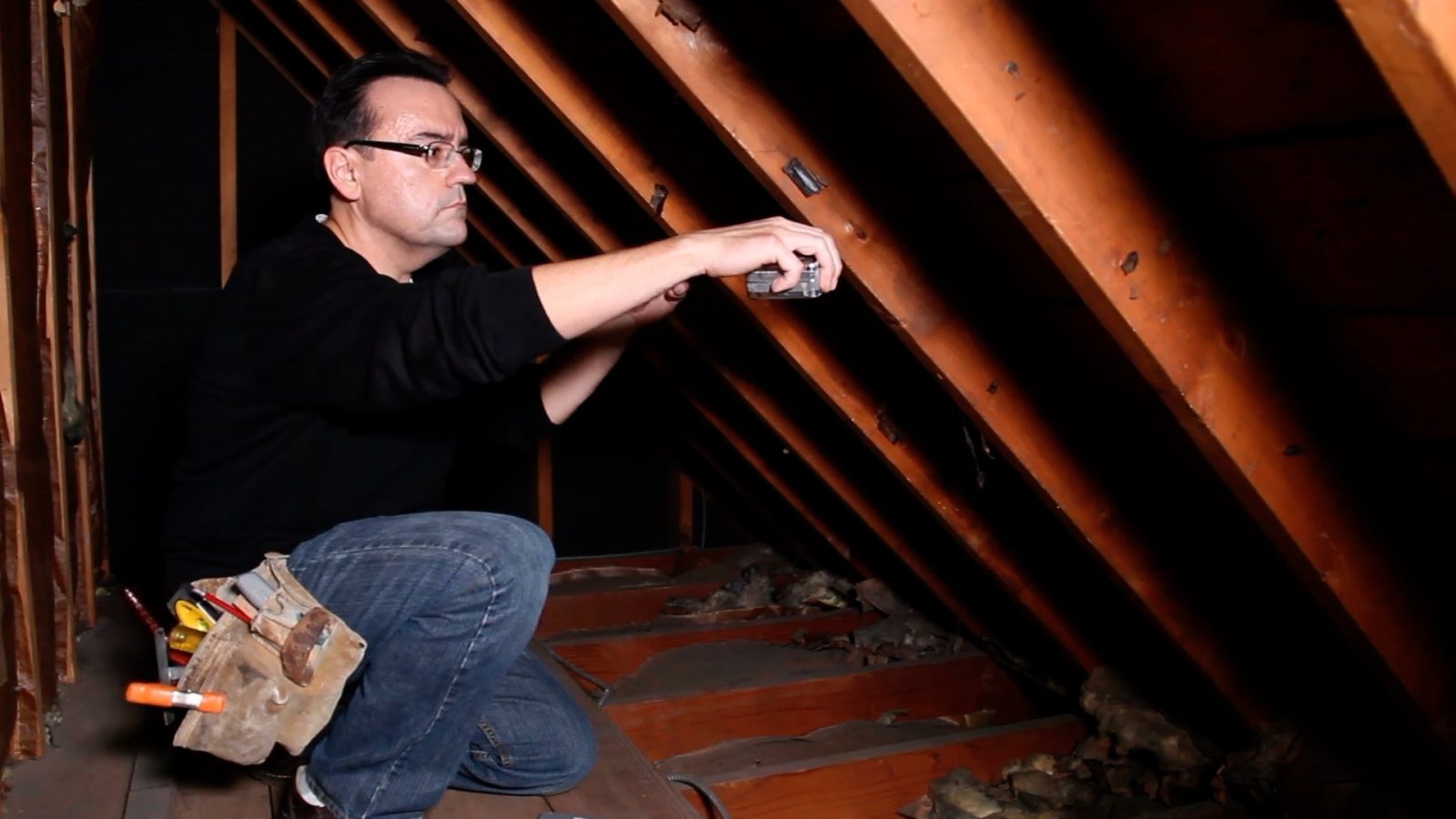a man measuring between studs along the inside of a roof line in an attic