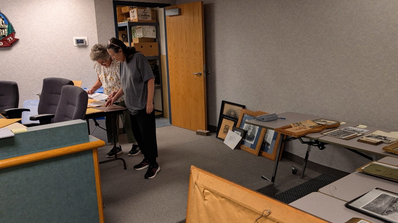two women pore over pictures and artifacts in the Osseo City Council chambers