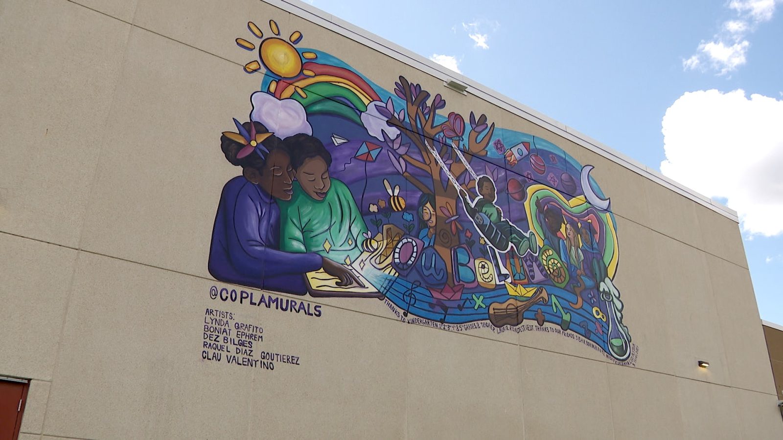 mural high atop the outside wall of a school building against a blue sky