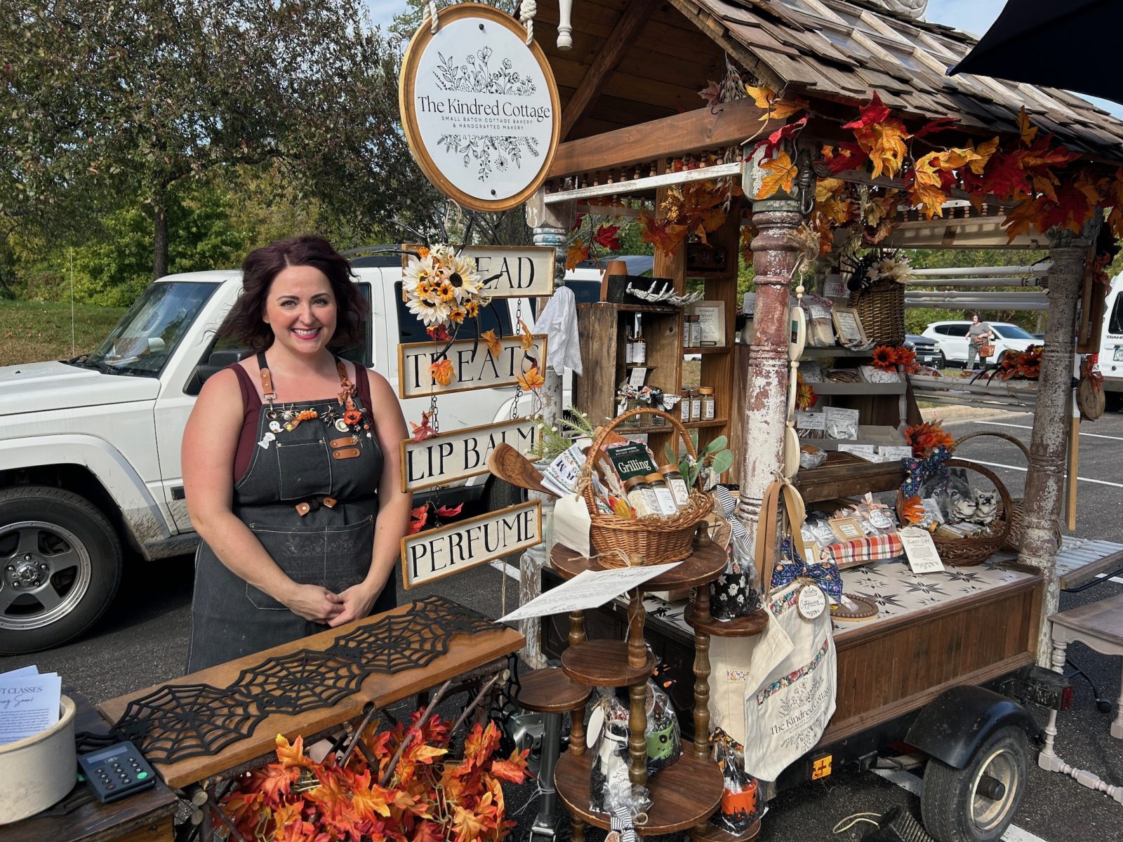 woman standing next to a cart filled with baked goods and arts & crafts.