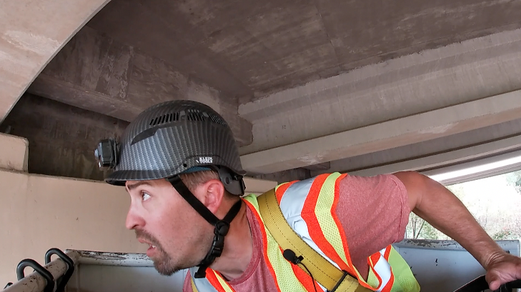 man wearing a helmet and a safety vest inspects a bridge
