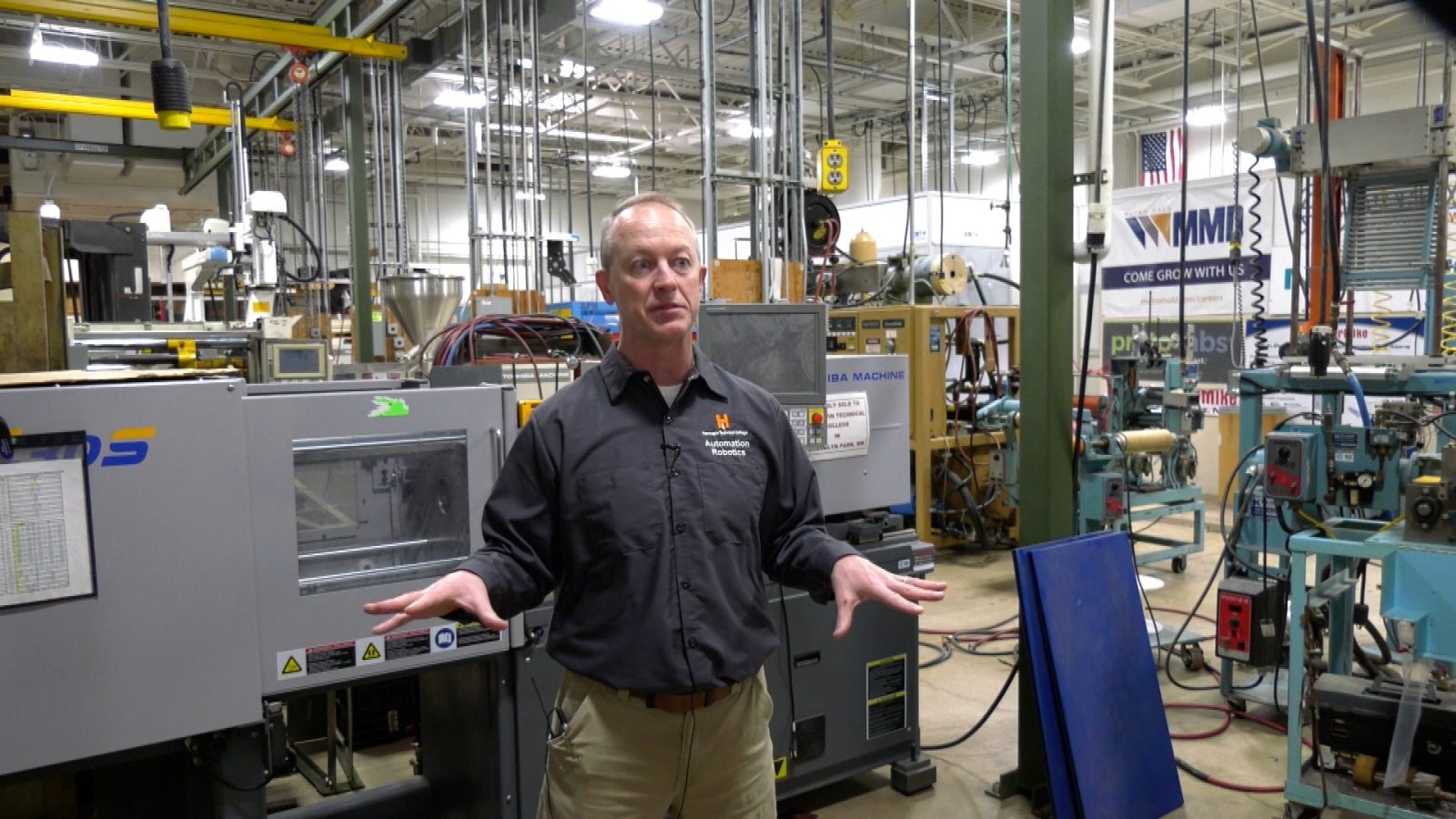 instructor in a Hennepin Tech button-up stands in front of a large machine