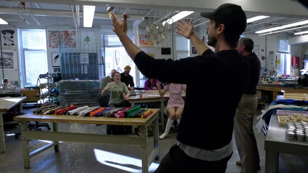Two men leading a classful of students with their arms up