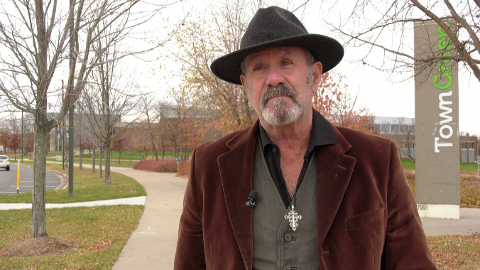 man with a goatee standing in a park wearing a hat