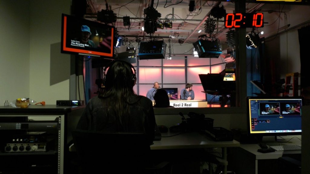 media control room, with people sitting at computers watching hosts sitting at a desk