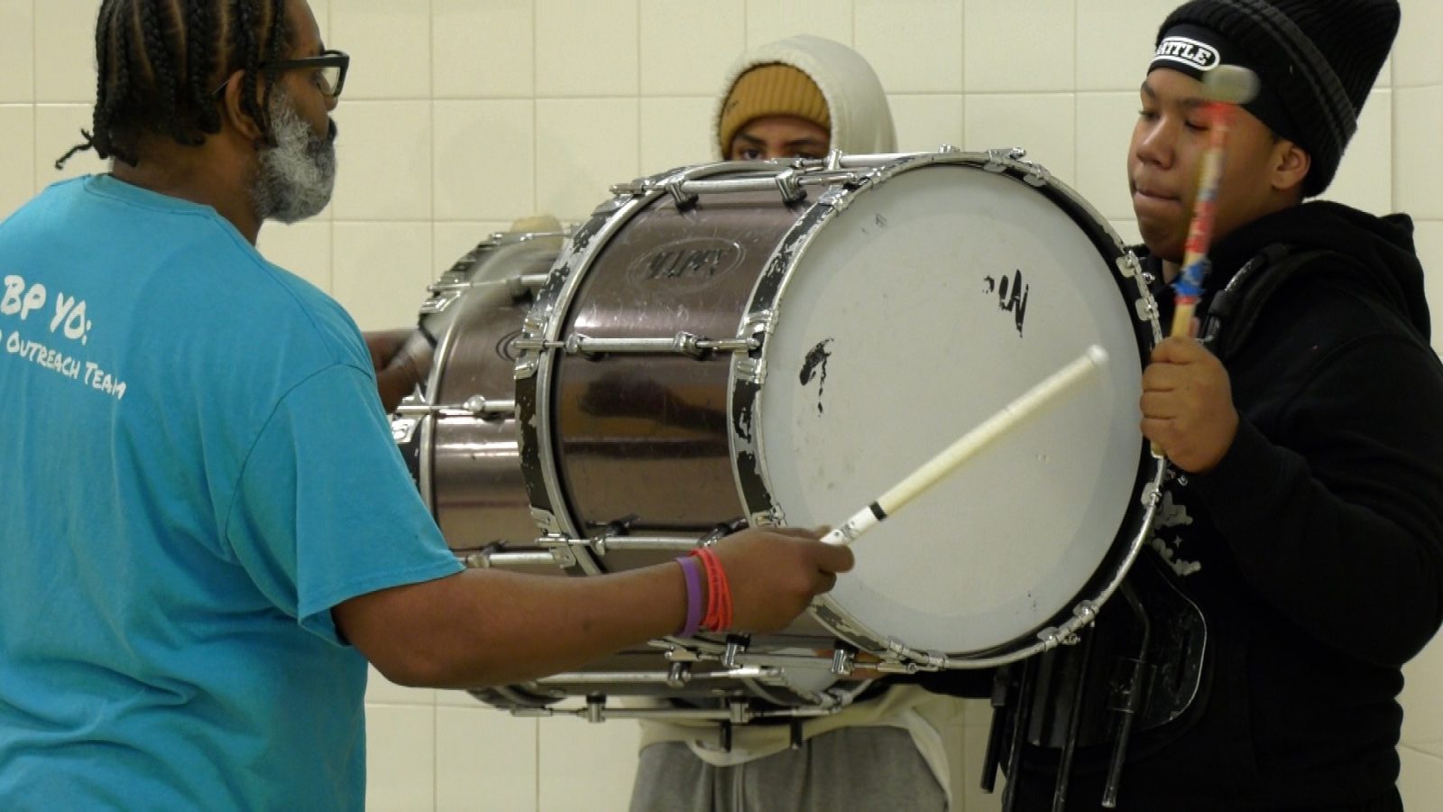 teacher drums on a bass drum with a student holding it