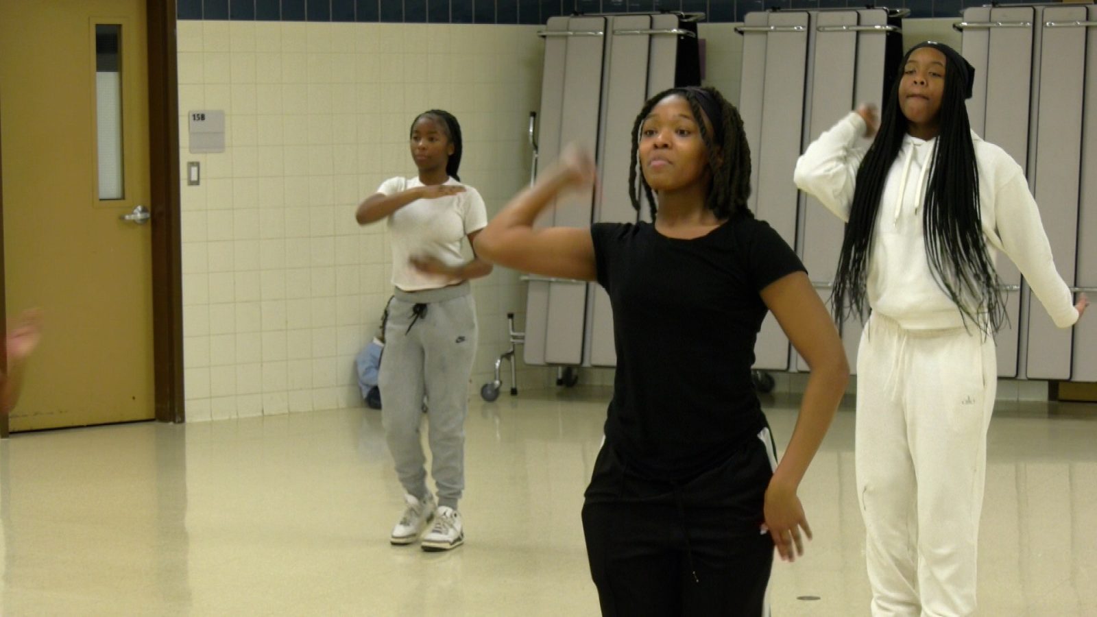 Three girls practicing a dance routine in a cafeteria