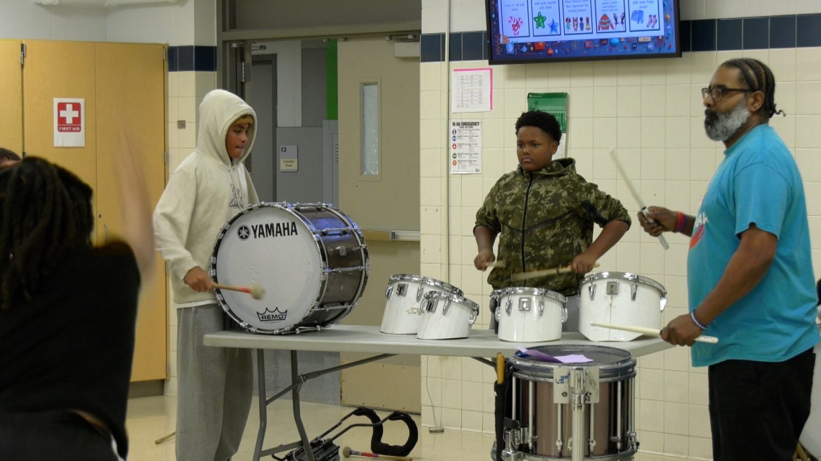 two kids and a teacher practice drumming while a dancer practices in the foreground