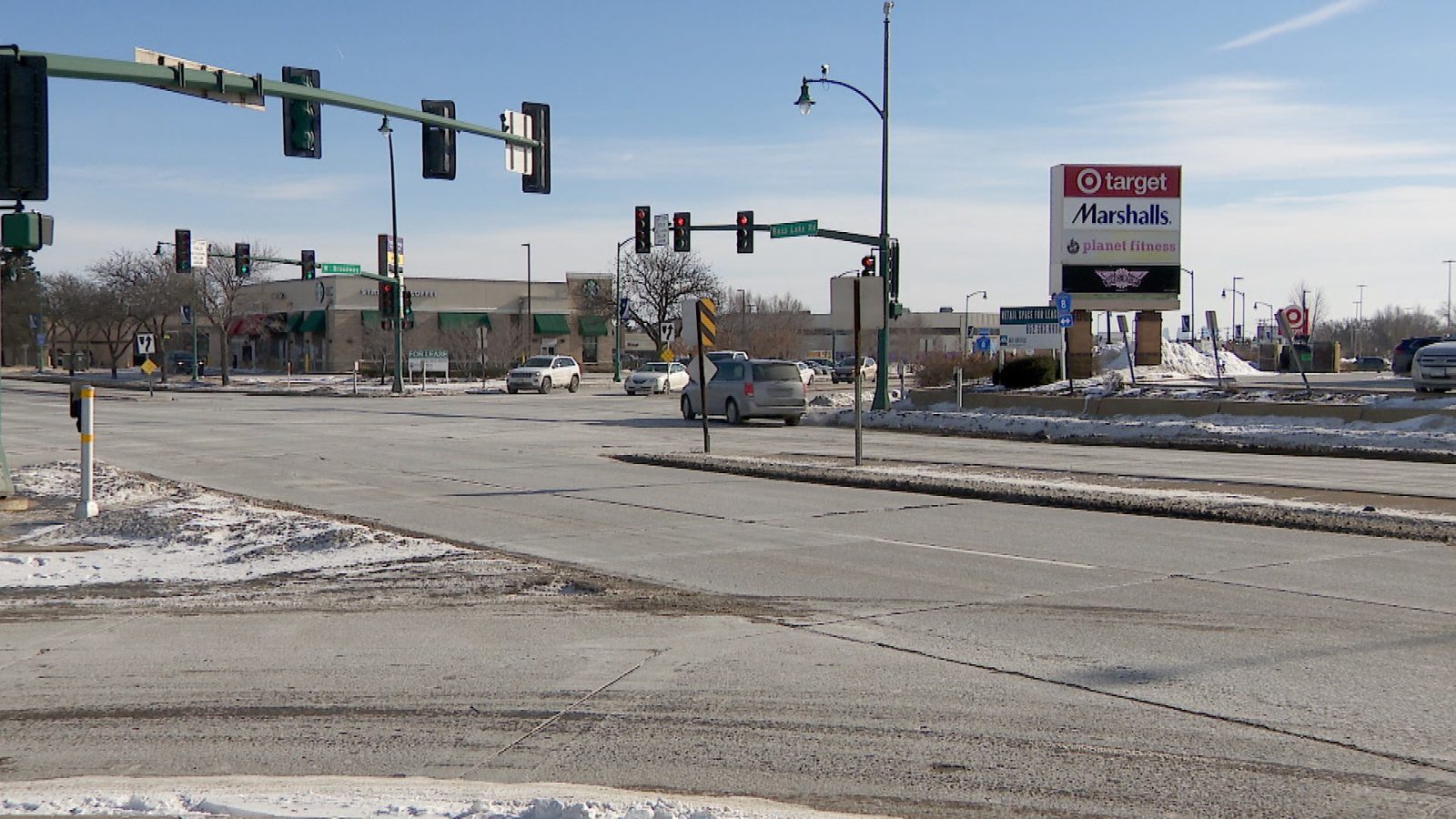 Cars travel through a snowy intersection on a sunny day