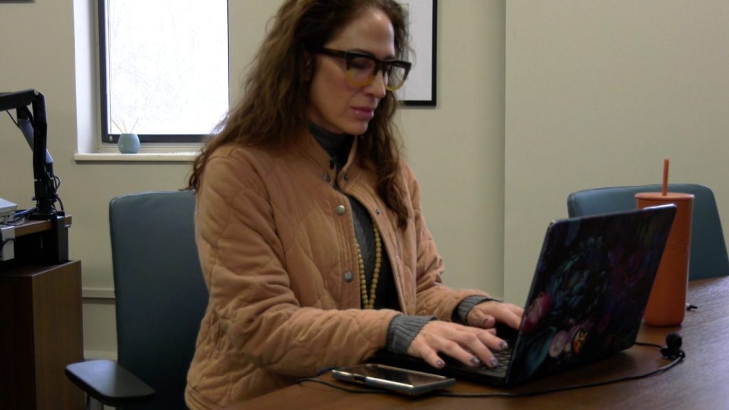 carly baker, brunette woman with glasses, works at laptop