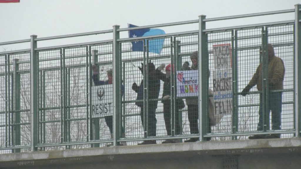 protestors with a variety of signs, including "resist," minnesota flag and a call to honk