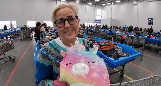 woman holds up a plush unicorn doll at a goodwill store