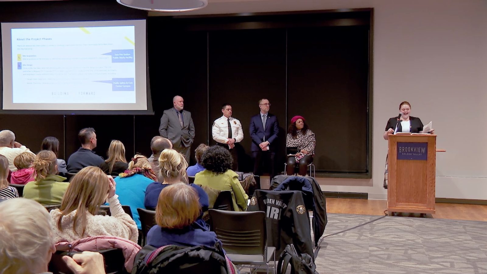 a panel of city leaders talk to a crowd in a ballroom