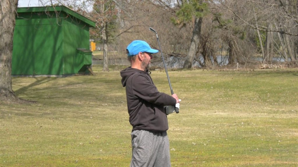 male golfer in a blue hat holding a golf club upright