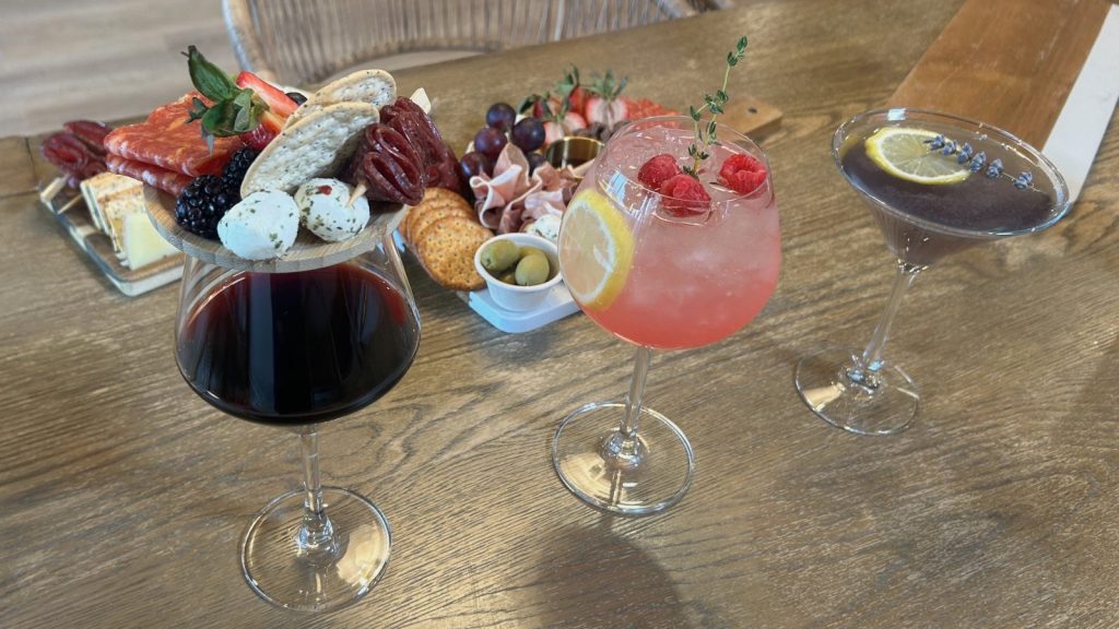three cocktails sitting in front of two charcuterie boards on a wooden table