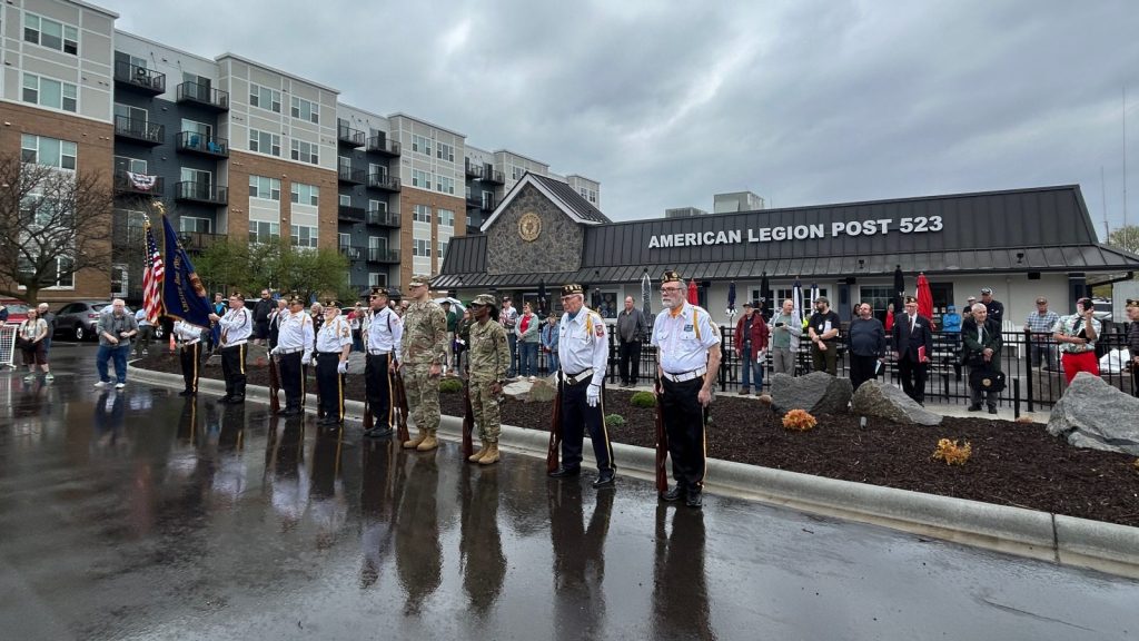 people lined up outside of an american legion post 523 building on a rainy day.