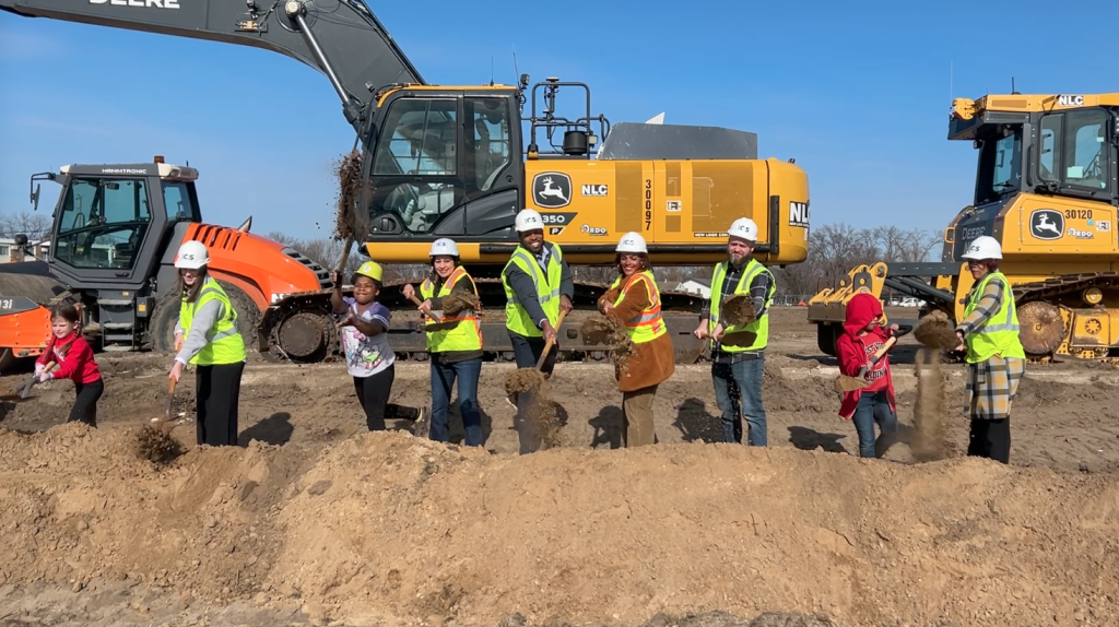 Osseo school board members and children at a groundbreaking event in front of construction equipment