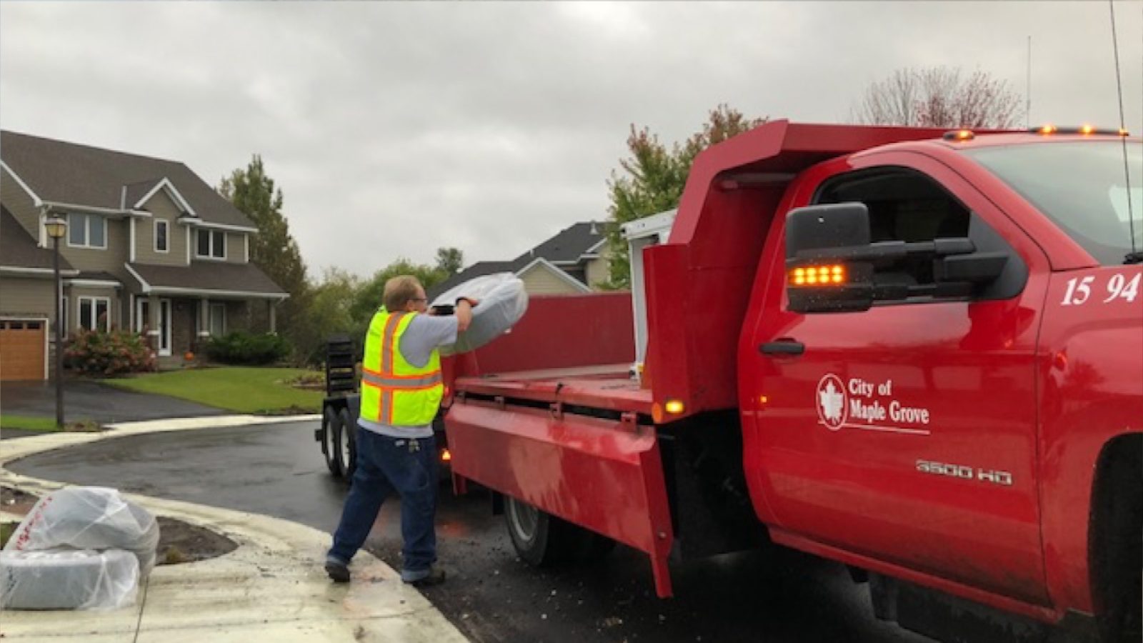a man loads a garbage bag containing a tire into the back of a rollback truck