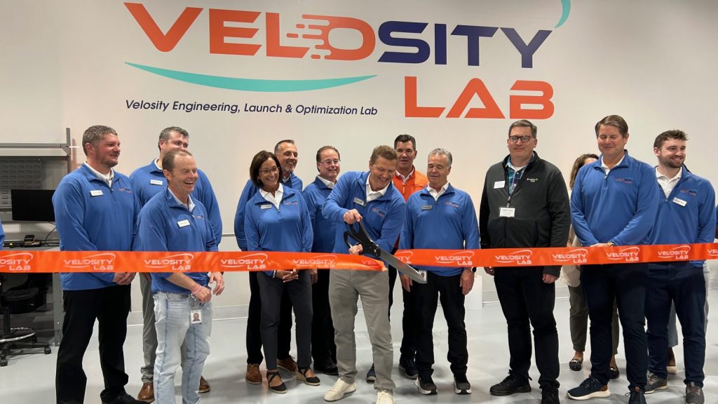 people in blue shirts cutting a ribbon next to a wall with Velosity Lab painted on it