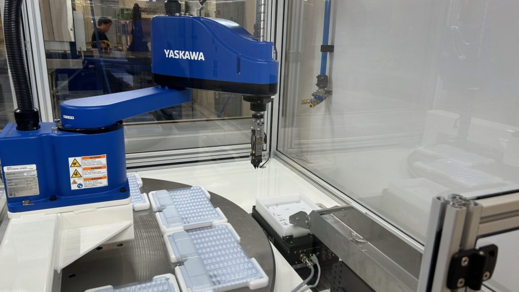 a blue robotic arm at velosity lab picking up small metallic pieces