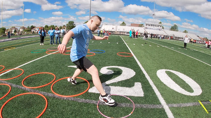 a student jumps through hula hoops on a football field at champlin park high school's unified track and field day