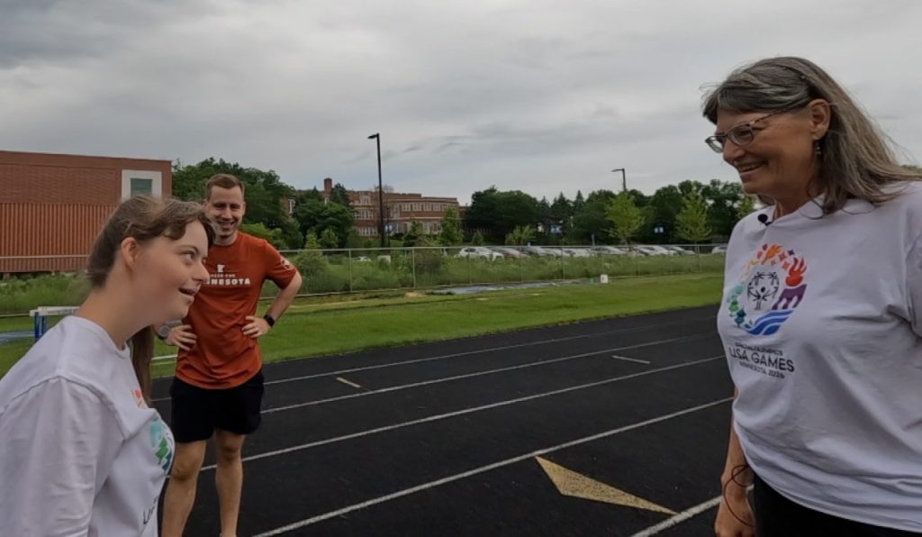 elizabeth, coach peter and her mom patty standing on a track looking at each other and smiling