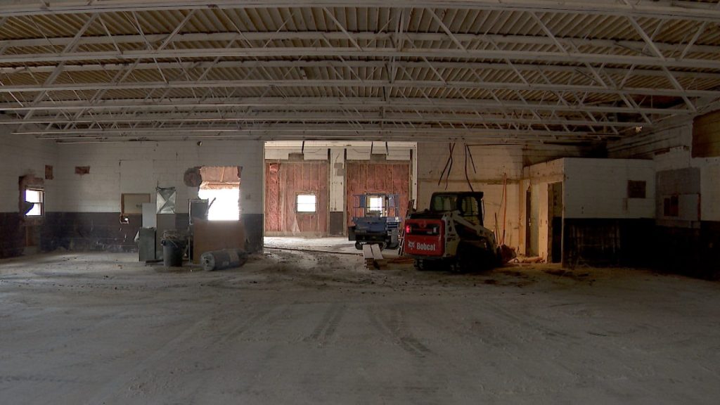 near-empty building with bobcat working inside it, exposed ceilings and stripped flooring and walls