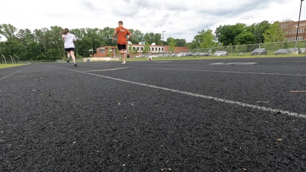 two people running on a track, photo taken from a low angle behind so most seen is the track