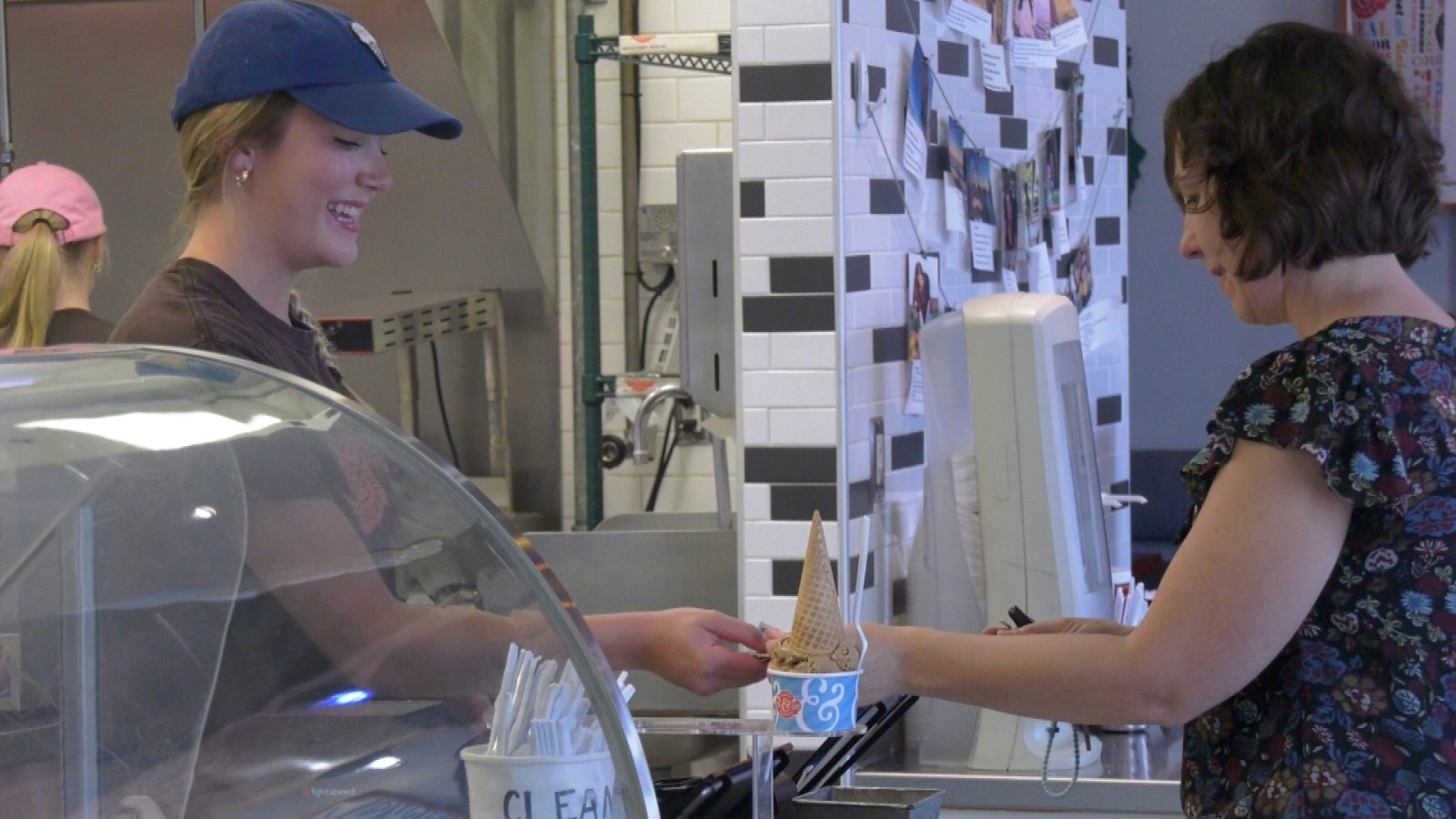 girl in blue hat helping customer at ice cream shop cash register